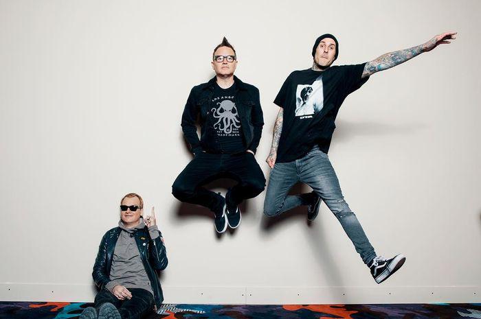 Blink-182 berpose di depan backdrop putih mengenakan pakaian serba monokrom